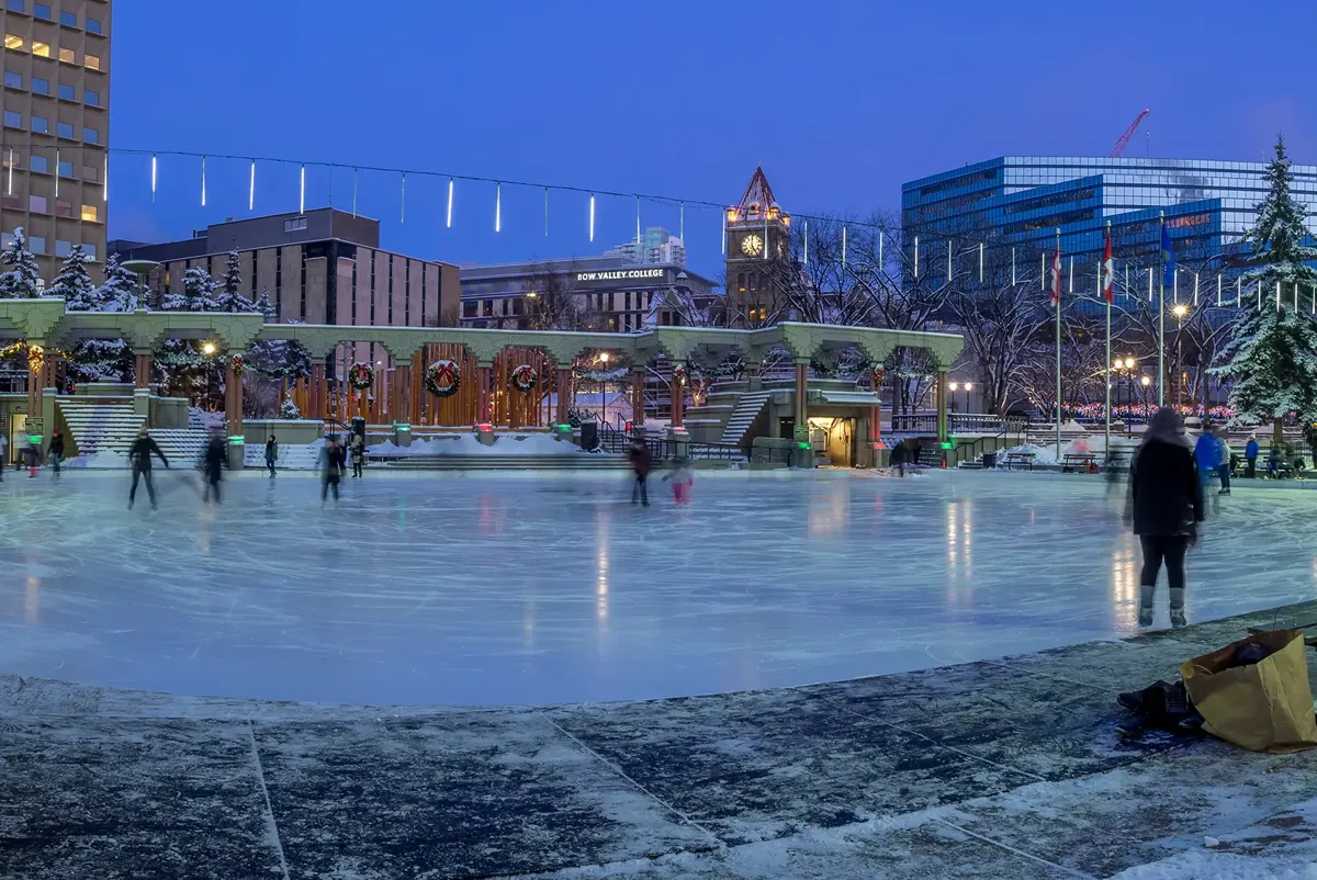 A large ice rink with people and buildings in the background.