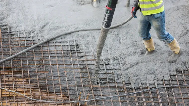 A person in a yellow vest and jeans working on a pipe.