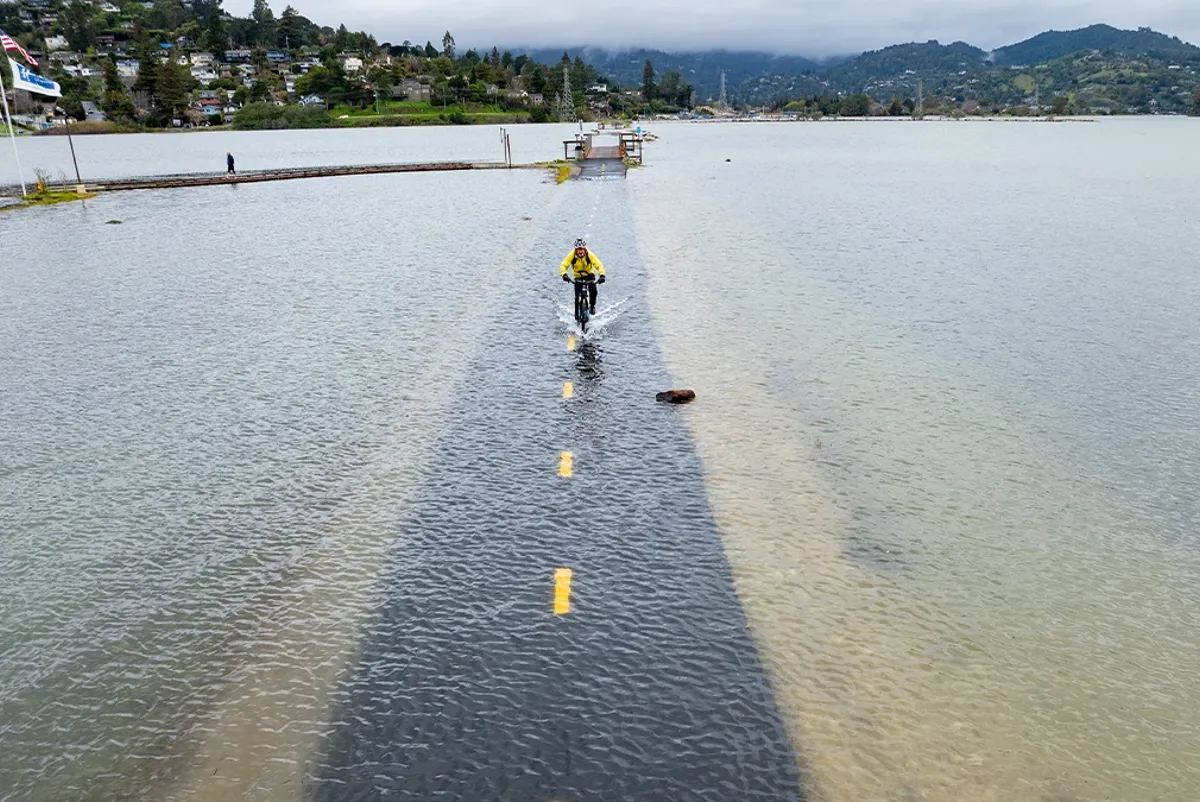 A person riding a bicycle through a flooded path on the coast of Marin County