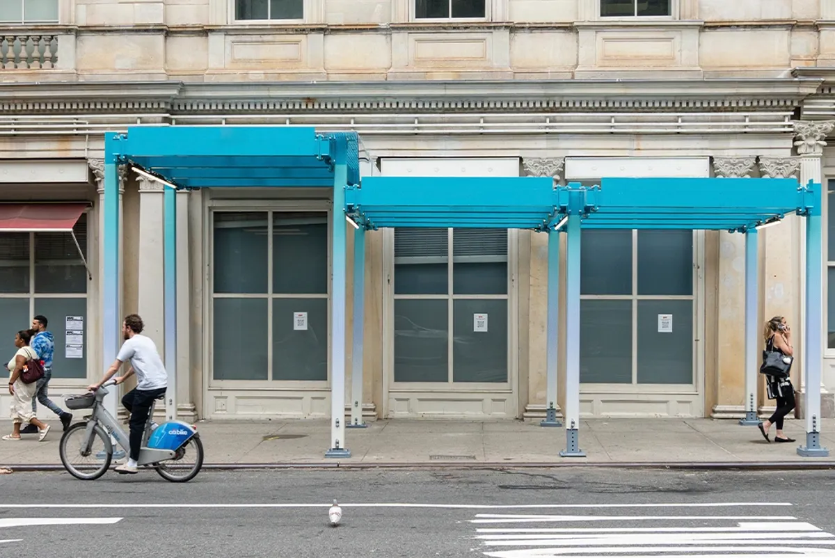 A person riding a bicycle past a blue sidewalk shed