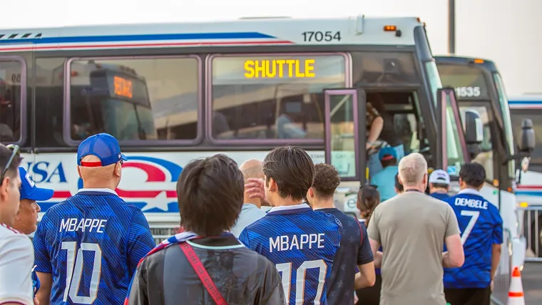 A group of people stand outside of a bus in soccer jerseys waiting to board