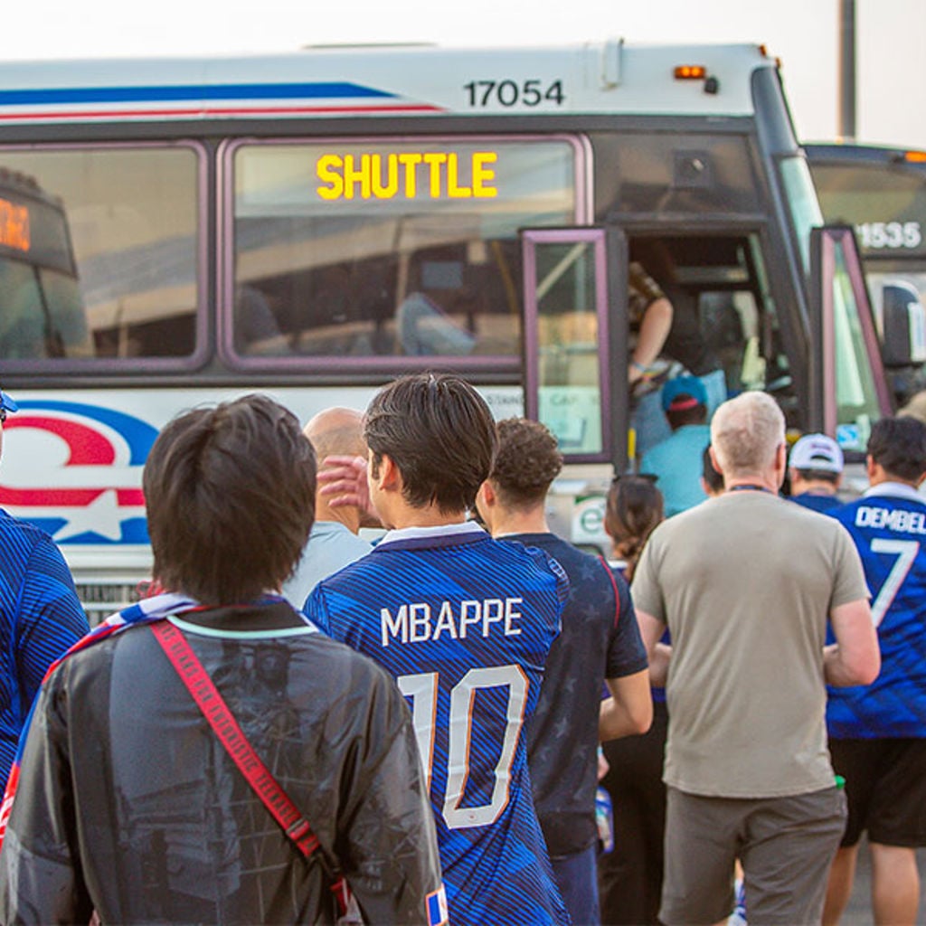 A group of people stand outside of a bus in soccer jerseys waiting to board