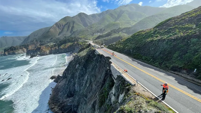 A road with a body of water and mountains on the side.