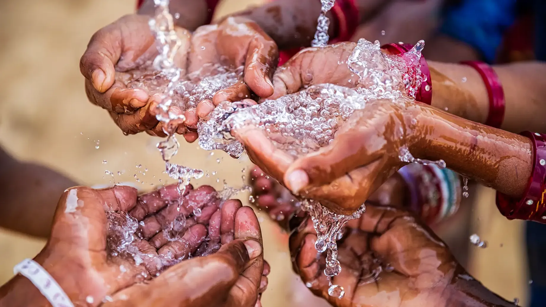 A group of hands cupping water flowing from a tap