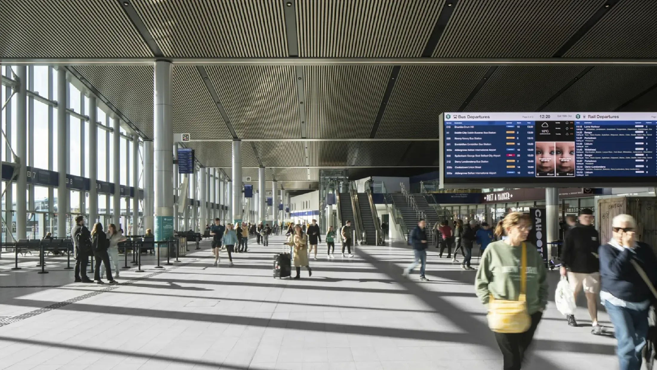 Travellers walking inside Belfast Grand Central Station, with large windows and daylight peeking through