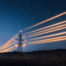 Electricity transmission towers with orange glowing wires in the night sky