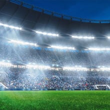 View from field of soccer stadium at night with crowd in distance and bright lights