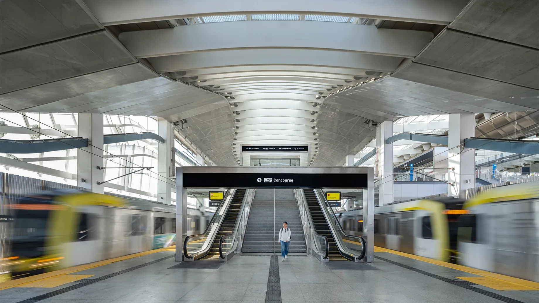 A person walking down a train platform with trains passing on either side