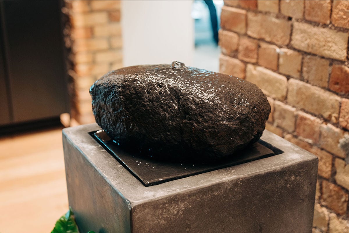 A large river stone featuring a low flowing waterfall inside an office. Credit: All Good Media