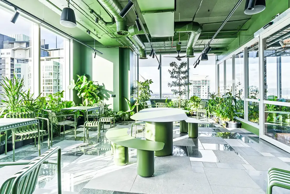 A room full of green plants, seats and tables, with green painted ceiling and wall to wall glass windows