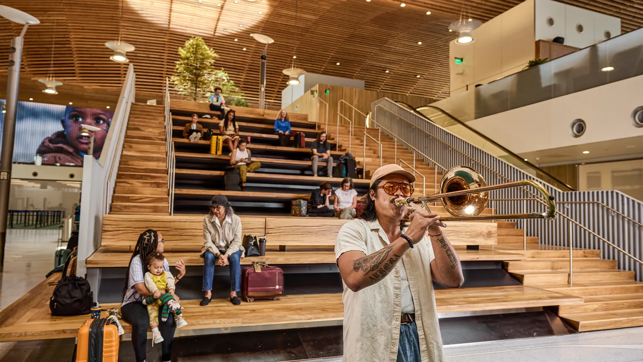 A person standing in a large room with people sitting on the stairs.