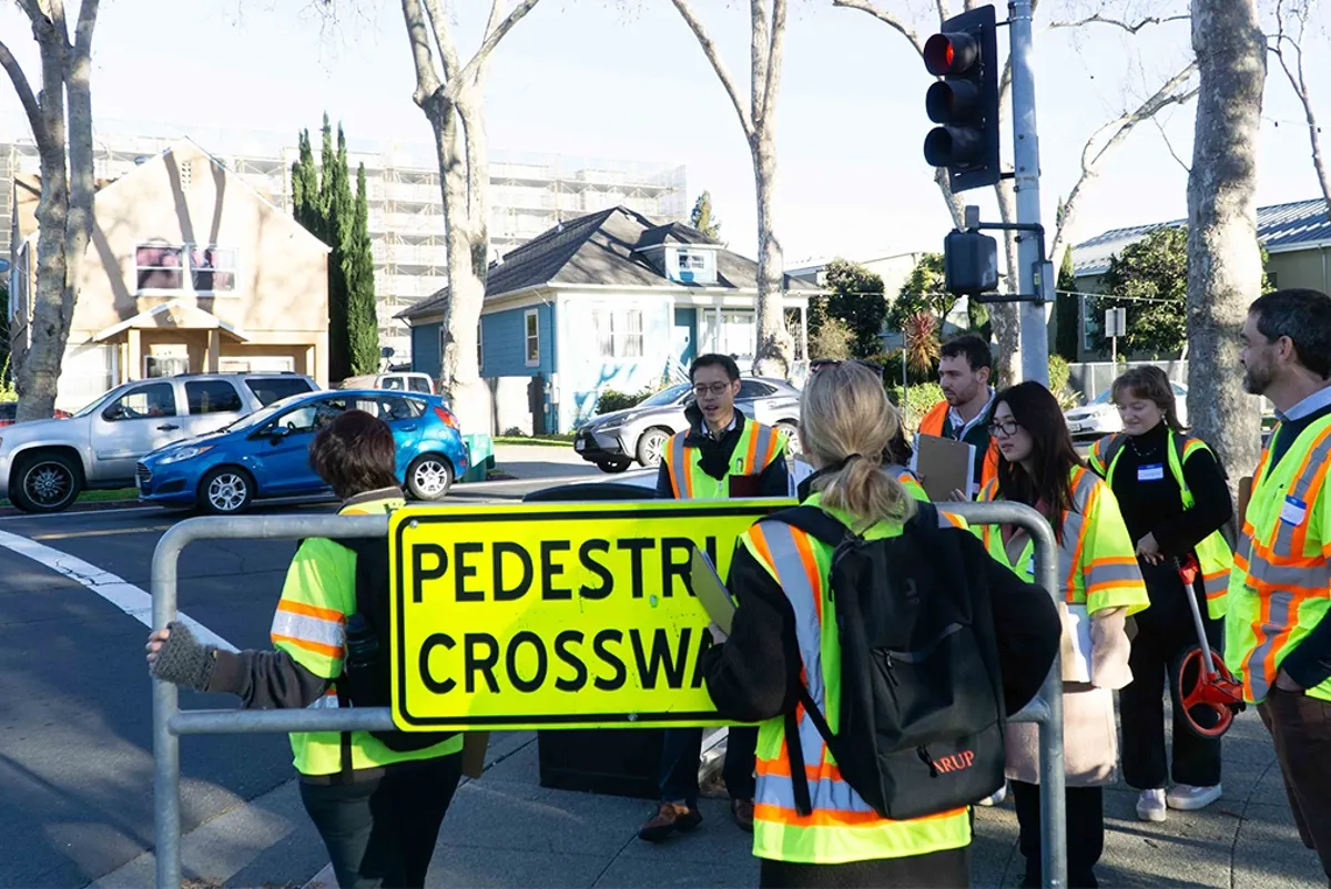 A group of people in safety vests waiting to cross the street