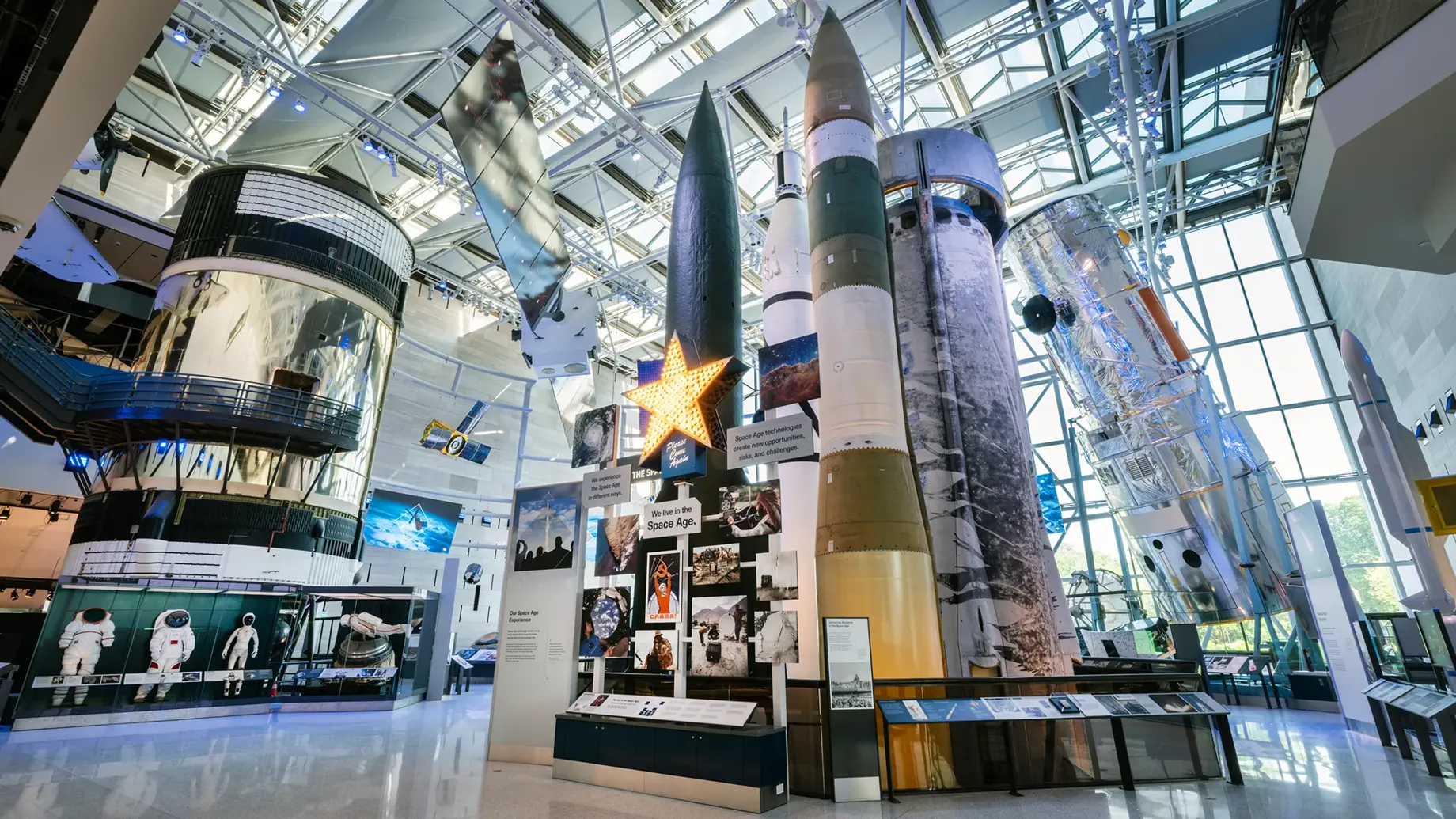 Shuttles and other large space science artifacts in bright windowed exhibit hall.