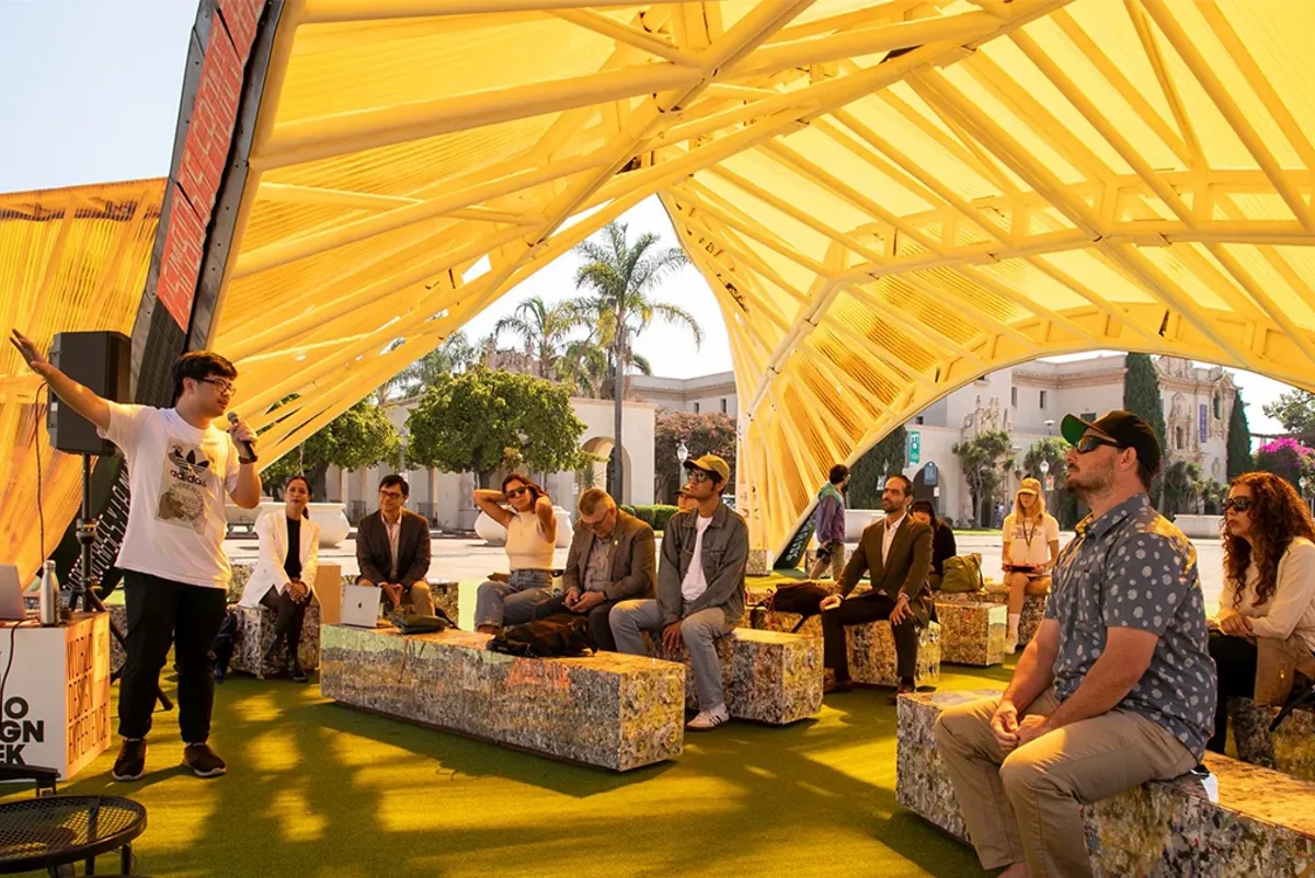 A person giving a presentation to a group of people outdoors under a yellow tent